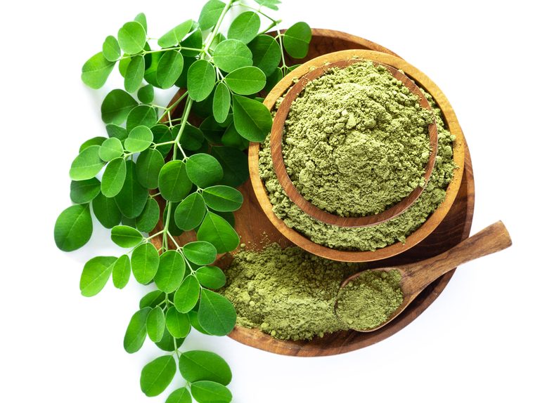 Moringa powder (Moringa Oleifera) in wooden bowl with original fresh Moringa leaves isolated on white background.